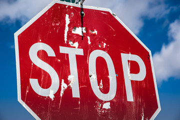 Looking up at a red stop sign full of bullet holes with dark blue sky and white clouds in the...