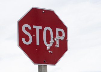 Red stop sign full of bullet holes with a background of white to grey clouds.  