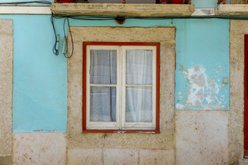 Square window on a pale blue, wheathered facade in Lisbon, Portugal.
