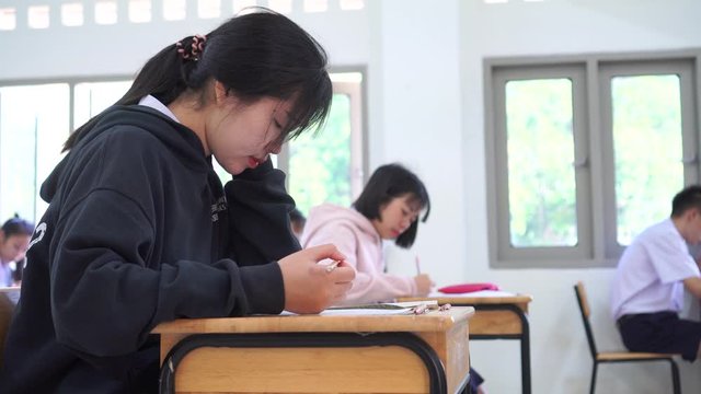 Test in high school /university student in exam room concept, Young Asian students group writing test paper answer sheet and sitting on taking final examination in classroom with concentration
