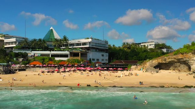 Dreamland beach one of the most beautiful sand beach Bali with happy travel tourist resting under umbrella and surfers in crystal clear sea water. Aerial view. Shot in 4K on Hasselblad, H.265
