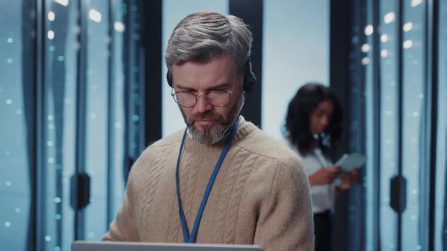 Professional IT businessman networking on laptop computer doing deep diagnostics for data processing inside secure server room. Male portrait.