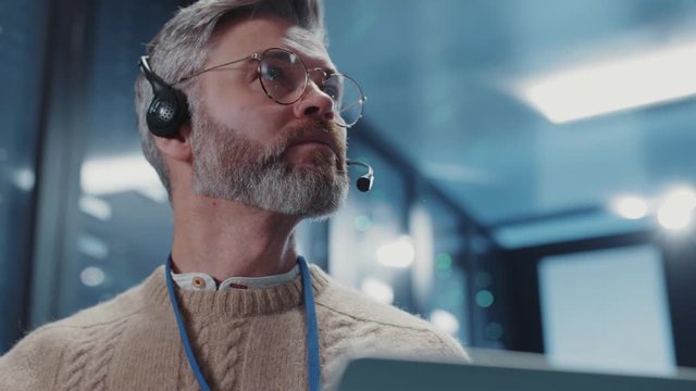 Portrait of experienced IT technician using laptop for work in server room. Close-up server administrator cloud computing backup network operations at data center.