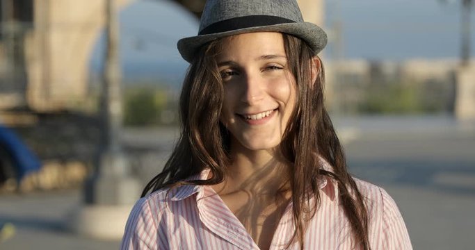 Portrait of beautiful teenager young girl with a hipster hat looking at camera and smiling sweetly at su set in the city. Spring and summer in Cagliari, Sardinia, Italy, Europe.