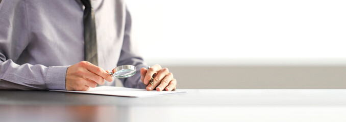 businessman in a tie is examining a document with a magnifying glass. Contract signing concept