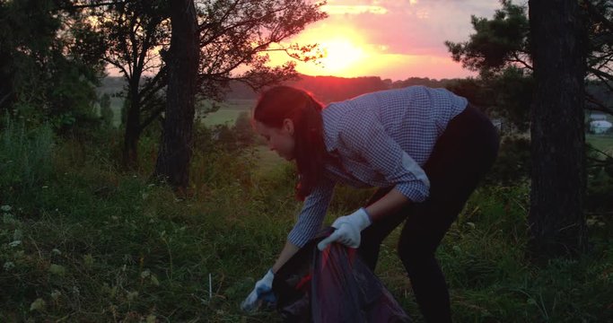 Cheerful young female volunteer collects plastic lied around the nature