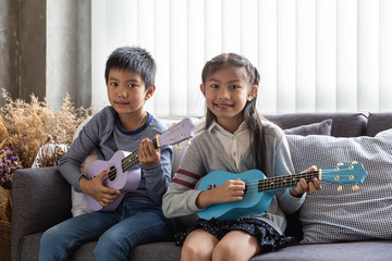 Children play ukulele happy in fun education,Little asia children sit on the sofa,intend to try...