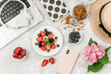Overhead view of laptop, fresh breakfast with fruit, headphones and mobile phone on white desktop table.Top view and flat lay. Woman business and breakfast concept.