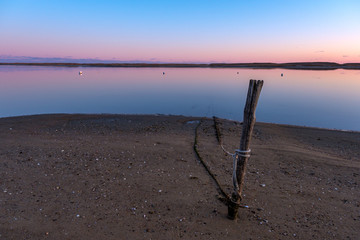 Sunset on an empty harbor, with a mooring line tied to a stake in the beach sand