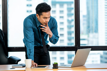 Young confident Asian businessman accountant office worker working with using laptop computer and digital tablet in modern office for success project. Young entrepreneur concentration work in office.