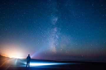 Fototapeta Adventurous man watching the stars on a beach at night.  obraz