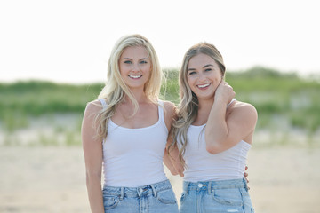 Two beautiful young female friends spend time at the beach in white tank top and denim
