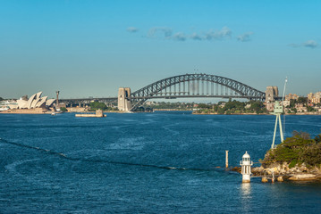 Fototapeta na wymiar Sydney, Australia - December 11, 2009: Long shot with Opera House and Harbour Bridge, metal span, bow and stone anchor towers against blue sky and above bay water. Some boats.