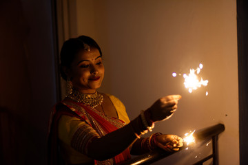 Young and beautiful Indian Bengali woman in Indian traditional dress is celebrating Diwali with fire crackers on a balcony in darkness. Indian lifestyle and Diwali celebration