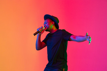 Young african-american musician singing on gradient orange-purple studio background in neon light....