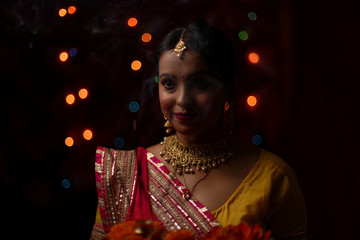 Close up portrait of young and beautiful Indian Bengali woman in Indian traditional dress celebrating Diwali with incense sticks and flowers in dark background.Indian lifestyle and Diwali celebration.