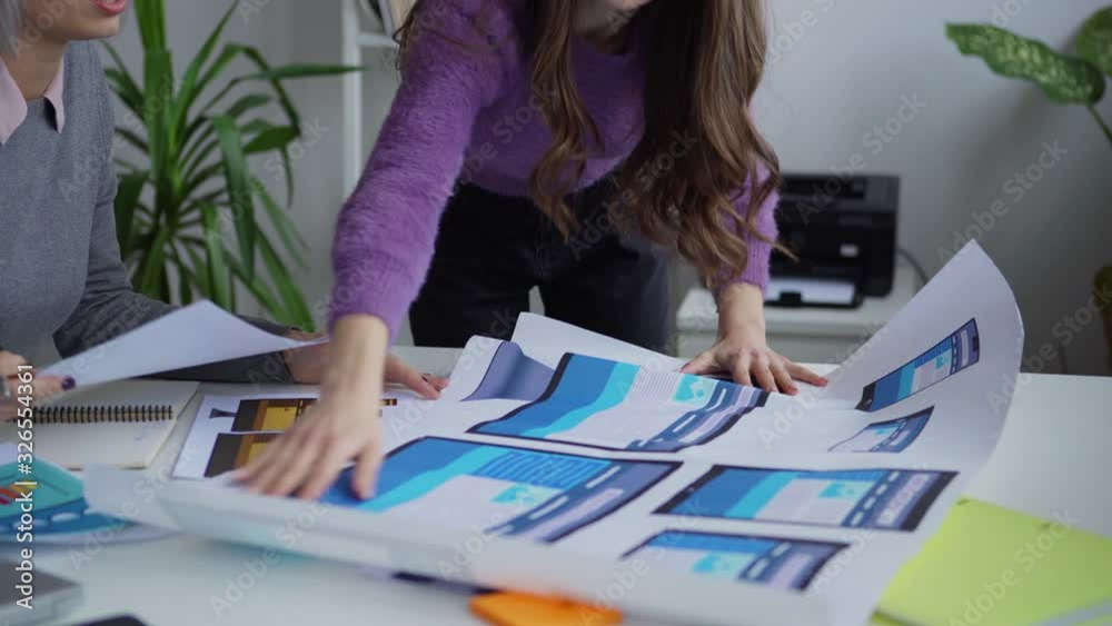 Wall mural young professional female web designers working with papers at table and discussing website design f