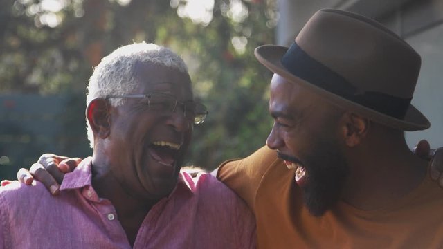Portrait Of Senior Father Talking And Laughing With Adult Son In Garden At Home