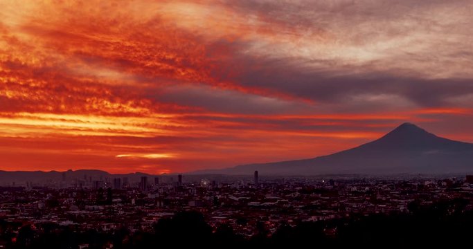 City of Puebla de Zaragoza overview at orange sunset with beautiful moving clouds and Popocatepetl volcano in background, motion time lapse.