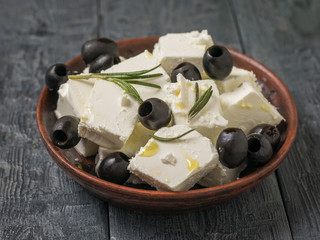Olives and herbs with slices of feta cheese on a wooden table.