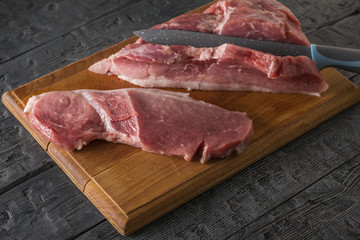 A large knife cuts steaks from a large piece of pork on a cutting Board.
