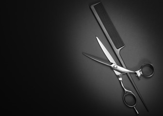 Scissors and comb. Beauty salon equipment. Shears for haircut on black background. Copy space, flat lay view - obrazy, fototapety, plakaty