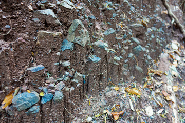 Layers of soil, or a wall of soil, with many blue rocks around the dark soil, close up.