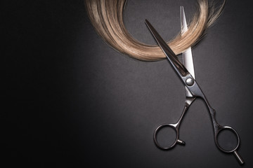 Scissors and piece of blond hair. Professional barber hair cutting shears on black background....