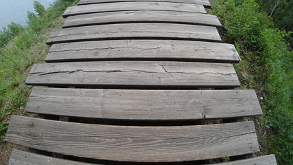 Wooden walkway through the forest. Green grass and shrubs. View from the top. Summer concept. Distortion wide angle shot.