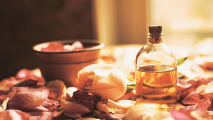 Essential aroma oil bottle among roses petals on wooden surface, toned warm, selected focus