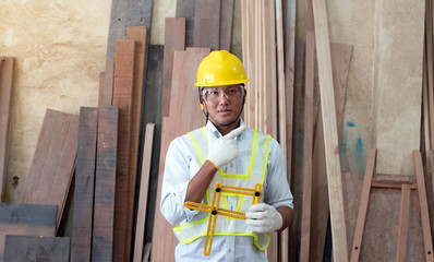 Handsome man wearing safety vest and yellow helmet,holding tablet in hand,posing in front of blurred wood pile,at factory,blurry light around