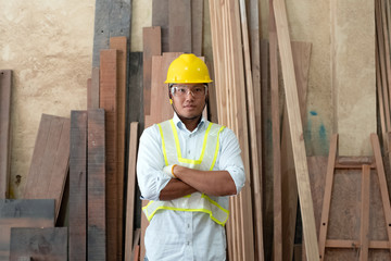 Handsome man wearing safety vest and yellow helmet,holding tools in hand,posing in front of blurred wood pile,at factory,blurry light around