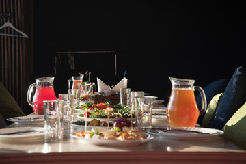 Table setting for a party or Banquet in a cozy small room. There are dishes and drinks on the table, and sofas with pillows are waiting for guests.