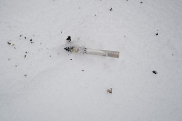 Environmental pollution. Cigarette butt thrown on white snow
