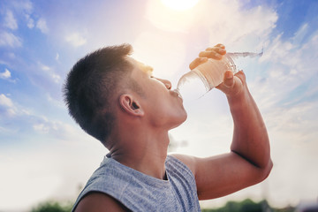 Runner man drinking pure water from plastic bottle after workout with sunrise background. Selected focus - obrazy, fototapety, plakaty