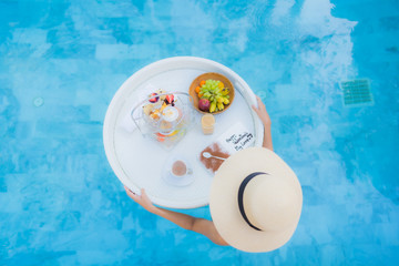 Portrait beautiful young asian woman enjoy with afternoon tea or breakfast floating on swimming pool