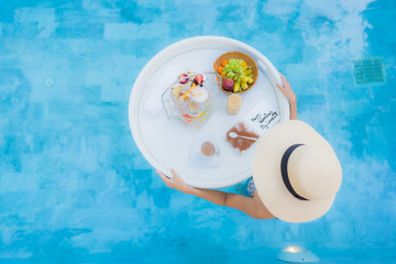 Portrait beautiful young asian woman enjoy with afternoon tea or breakfast floating on swimming pool