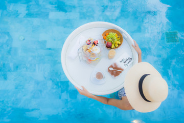 Portrait beautiful young asian woman enjoy with afternoon tea or breakfast floating on swimming pool