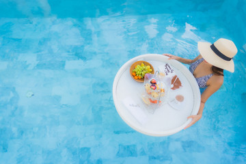 Portrait beautiful young asian woman enjoy with afternoon tea or breakfast floating on swimming pool