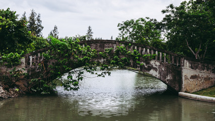 Fototapeta na wymiar Old vintage concrete bridge over the lake or pond water in public park.
