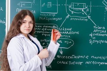 A student with a test tube in her hands is standing at the blackboard with chemical formulas. Fun time at the university.