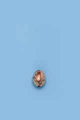 One gilded quail egg on a blue background.