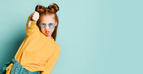 Red-haired teenager girl in smoked blue glasses and yellow sweatshirt is showing thumbs down sign gesture. Banner - obrazy, fototapety, plakaty