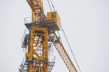 Naklejka premium A yellow construction crane is building a house out of concrete blocks against a blue sky