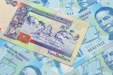 A close up image of a colorful two dollar bill from Belize with a pile of Mexican twenty peso bank notes in macro