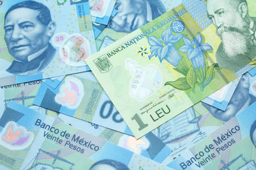 A close up image of a green Romanian one leu bank note on a background of Mexican twenty peso bank notes