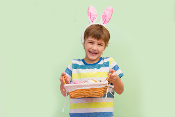 Cute little child boy wearing bunny ears holding basket with easter eggs poses on a green background.  Happy easter!