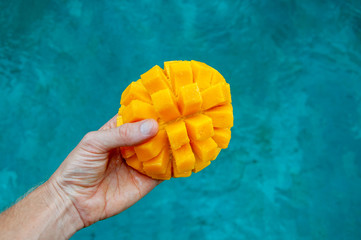 chopped juicy mango in hand on pool background