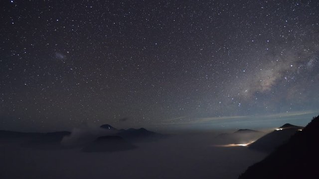 Time-lapse of the milky way over Bromo volcano with the sea of fog and the light from cars or vans at dawn in Java, Indonesia.