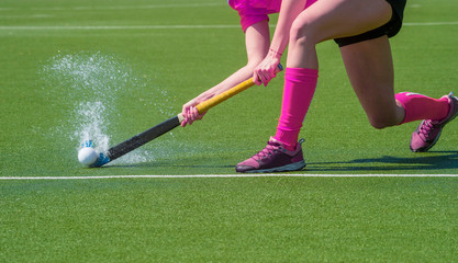 Female field hockey player passing to a team mate on a modern, water artificial astroturf field